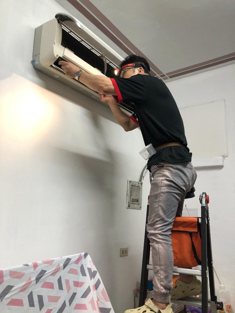 飛揚清洗技師站在梯子上到府清洗壁掛式分離冷氣，現場已鋪防護布